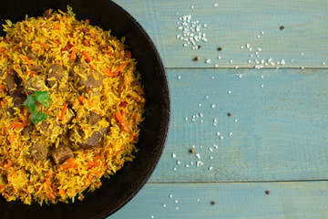 Dish of oriental cuisine - pilaf with lamb in a pan, on a wooden background.