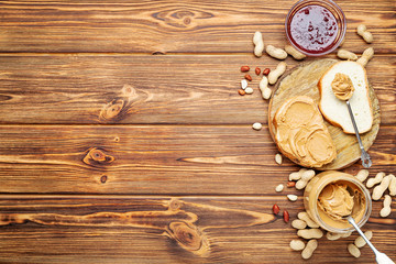 Toast sandwich with peanut butter. Spoon and jar of peanut butter, jam and peanuts for cooking breakfast on a brown wooden background. Flat lay with place for text.
