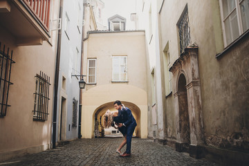 Stylish couple dancing in european city street on background of old architecture. Fashionable man and woman in love dancing with passion in city. Traveling together in Europe