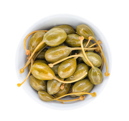 Pickled capers with cuttings in a porcelain bowl. Top view close up.