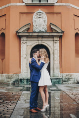 Stylish couple embracing together in european city street on background of old architecture. Fashionable man and woman in love enjoying day in city. Traveling together in Europe