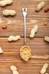 Vintage spoon with creamy peanut butter on a brown wooden table. Near the peanut butter lies peanuts in the shell and peeled peanuts. Flat lay of peanut paste for cooking breakfast.Vegan food concept
