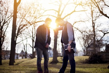 Men discussing the bible in a garden under sunlight with a blurry background