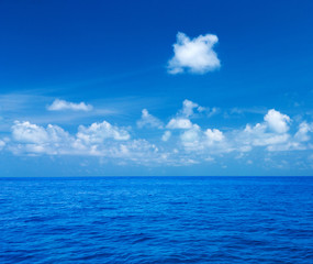 Naklejka na ściany i meble Sea and blue sky. Blue sea water and sky with white fluffy clouds. Horizontal background of blue sea. Tropical landscape