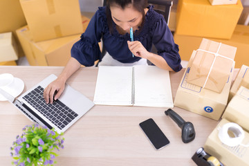 Top view, Asian women who are SME online shopping operators and are writing lists on notebooks SME online shopping business entrepreneurs or independent work concept