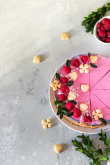 Raspberry cream mousse cake (no baked cheesecake) decorated with fresh raspberries, mini cookies and coconut flakes on light grey background.