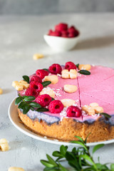 Raspberry cream mousse cake (no baked cheesecake) decorated with fresh raspberries, mini cookies and coconut flakes on light grey background.