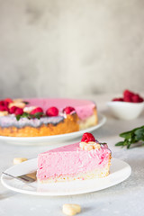 Raspberry cream mousse cake (no baked cheesecake) decorated with fresh raspberries, mini cookies and coconut flakes on light grey background.