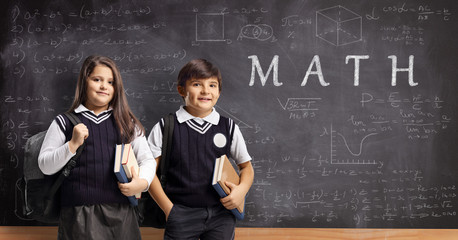 Schoolboy and schoolgirl in uniforms standing in front of a chalkboard with math formulas