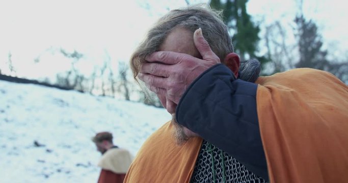 Sad chieftain wipes forehead and looks on killed troops on snow after fight