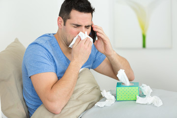 man coughing covering mouth with a tissue at home