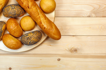 Loaves of bread and rolls on a plate on a wooden background