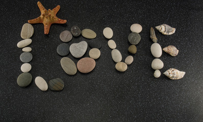 Word LOVE made of sea smooth stones and seashells on black granite with white spots background with starfish