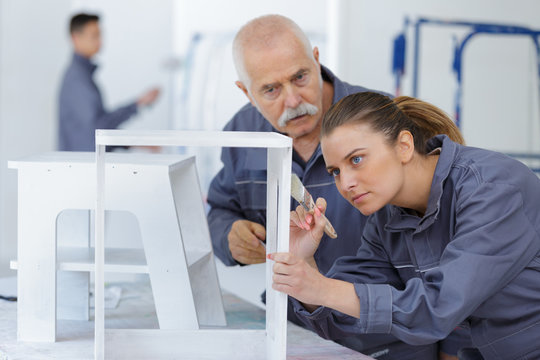 mature man teaching woman how painting a white furniture
