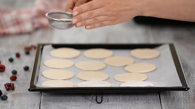 A baker uses a sifter to sprinkle powdered sugar on puff pastry. Making French Mille Feuille at kitchen.