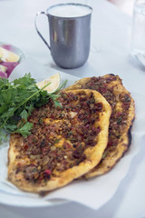 Thin turkish pita bread covered with minced meat and onions on a table with lemon and parsley, close up