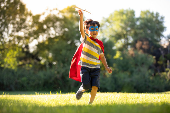 Little Boy In Superman Costume Playing On Meadow