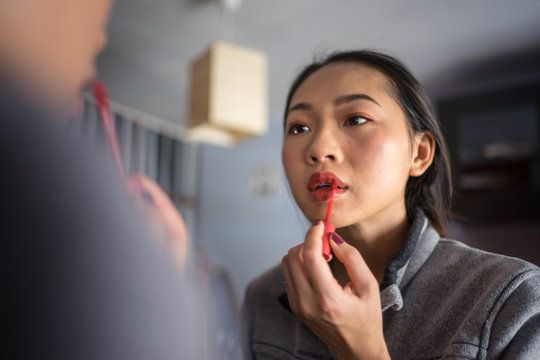 Young woman applying lipstick in front of mirror