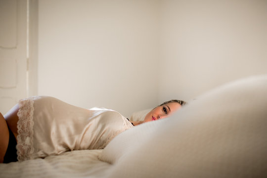 Side view of pregnant woman in underwear relaxing on comfortable bed at home