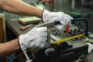 Crop anonymous professional male repairman in gloves sawing metal details with hacksaw during work in factory