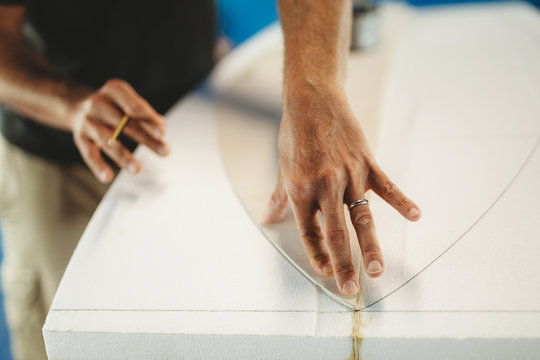 Crop professional male with pencil in hand circling pattern of surf board while working in workshop