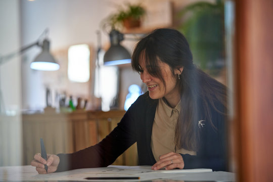 Woman sitting at a table with a pencil drawing jewels on paper