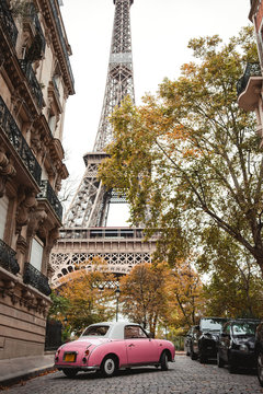 From below Eiffel Tower and pink antique car in street of France in fall