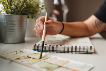Closeup of unrecognizable woman using palette and watercolors while creating picture and sitting at table at home in Paris