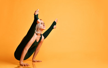 Blonde athletic girl trainer doing yoga pose asana stretches in sport fitness gym club in green...