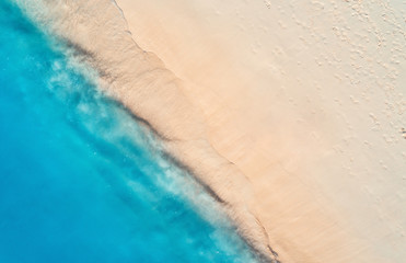 Aerial view of transparent blue sea with waves and empty sandy beach at sunset in summer holiday in Zanzibar, Africa. Tropical landscape with lagoon, white sand and clear ocean. Top view from drone