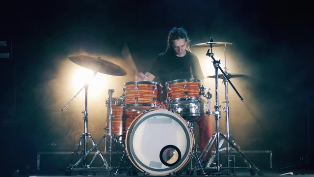 Dark studio with a male musician playing the drum set in it
