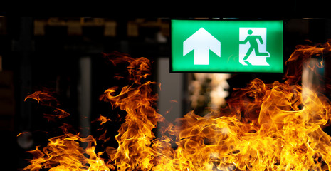 Hot flame fire and green fire escape sign hang on the ceiling in the Warehouse at night. The...