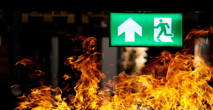Hot flame fire and green fire escape sign hang on the ceiling in the Warehouse at night. The concept of fire escape training and preparation for evacuation