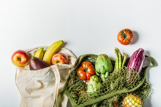 Fresh vegetables in a green string bag and fruit in a bag made of natural materials, eco-friendly product on a light gray background. No plastic.