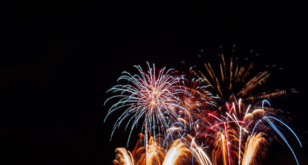 Gold fountain fireworks with red highlights below white starburst fireworks with a black background