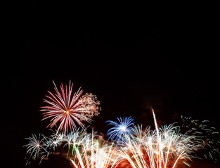 Red starburst, blue starburst over gold and white fireworks with a black background