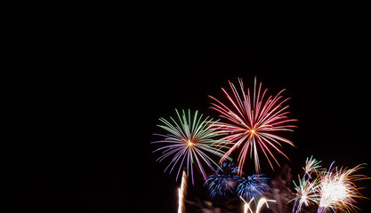 Green, red, blue, and white starburst fireworks against a black background