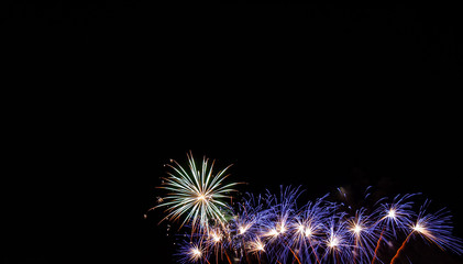 Blue starburst fireworks with white centers and a large white and orange starburst with a black background