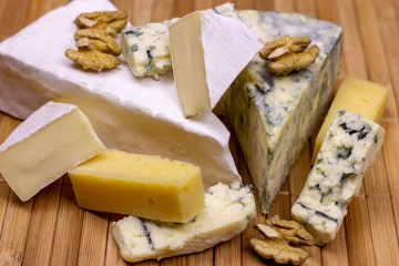 Many different varieties of cheese: blue, brie, camembert and other with walnuts on wooden board background.