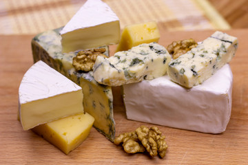 Many different varieties of cheese: blue, brie, camembert and other with walnuts on wooden board background.