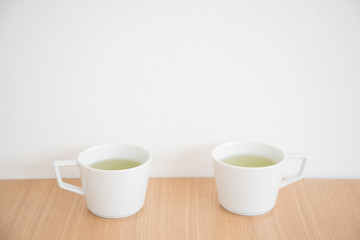 シンプルなマグカップに入れた緑茶　２つ　2人　２人　ふたり　二人　余白　ホワイトスペース　文字スペース　コピースペース　空白　背景　背景素材　グラフィック背景　グラフィック素材　木目　木　テーブル　机　上