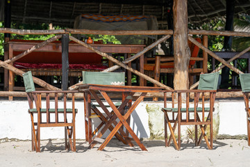 Fototapeta na wymiar Wooden table and chairs near sea on the tropical sand beach. Outdoor restaurant at the beach on the island of Zanzibar, Tanzania, Africa