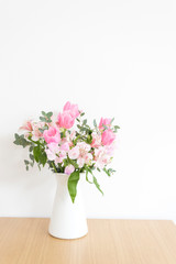 シンプルな花瓶とピンク系の花　ピンク系の花とグリーン　部屋　白壁　白背景　室内　屋内　自然光　余白　ホワイトスペース　コピースペース　文字スペース　縦　背景素材　背景　グラフィック素材　　白　緑　ピンク　春　季節　スイートピー