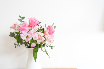 ピンク系の花とグリーン　白い壁　室内　部屋　屋内　アレンジメント　花束　花　春　ピンク　観葉植物　華やか　爽やか　春らしい　かわいい　おしゃれ　白背景　文字スペース　コピースペース　ホワイトスペース　余白　横位置