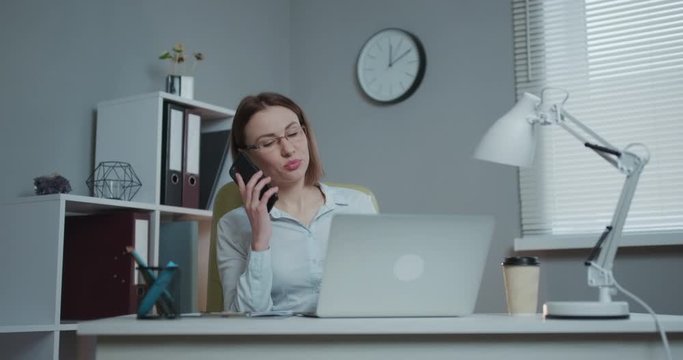 Attractive woman in eye glasses enjoying her favourite freelance job working in home on laptop computer. Female freelancer using smartphone, netbook and writing ideas in notepad