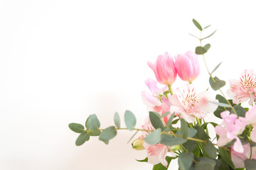 Fototapeta na wymiar シンプルな花瓶とピンク系の花　ピンク系の花とグリーン　部屋　白壁　白背景　室内　屋内　自然光　余白　ホワイトスペース　コピースペース　文字スペース　縦　背景素材　背景　グラフィック素材　　白　緑　ピンク　春　季節　スイートピー