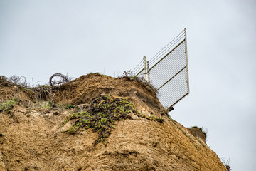 USA, California, San Mateo County, Half Moon Bay. A barwire fence hangs off the edge of a cliff...