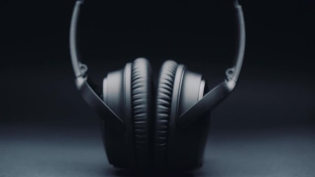 A product shot of headphones on a black background, standing upright. Camera movement from wide to a close-up plan. Focus shifting, top light.