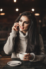 Woman talking on phone and drinking coffee in a cafe.