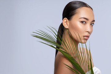 Naklejka premium Cute Asian lady looking at camera with tropical leaf